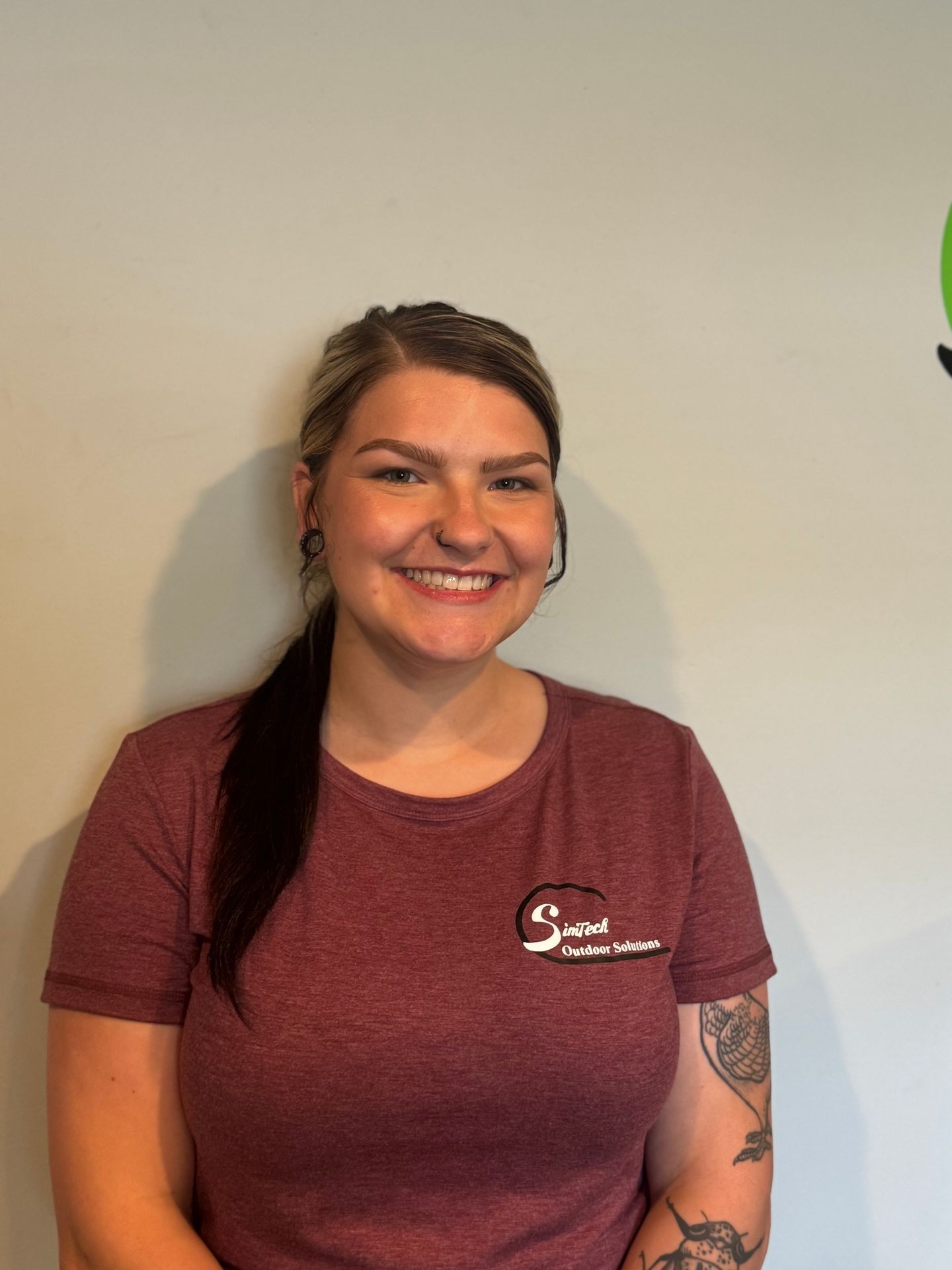 Smiling person in a maroon shirt with tattooed arm against a plain background.