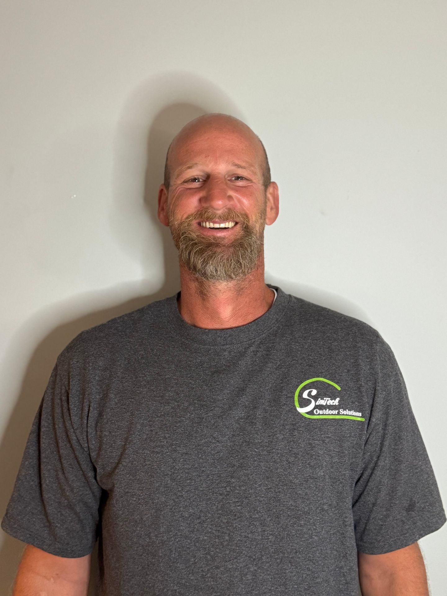 Smiling man in a gray shirt with 'Outdoor Solutions' logo against a plain background.